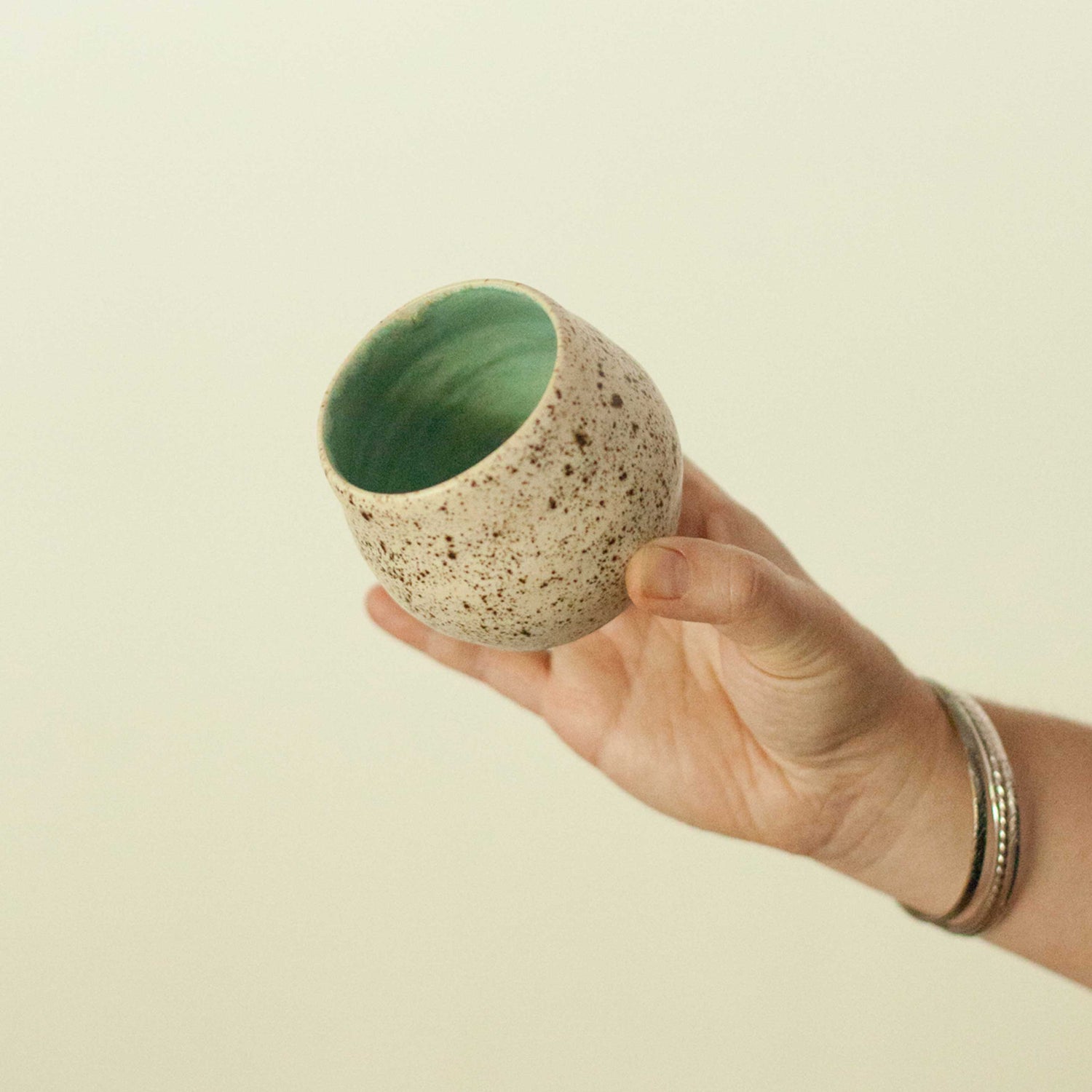 Holding a handmade pottery mug, the angle shows the detail inside the mug which is a green glaze wash, while the outside has a speckled cream glaze