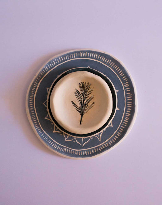 Three handmade pottery plates stacked on top of each other with an etched design and pattern and blue glaze