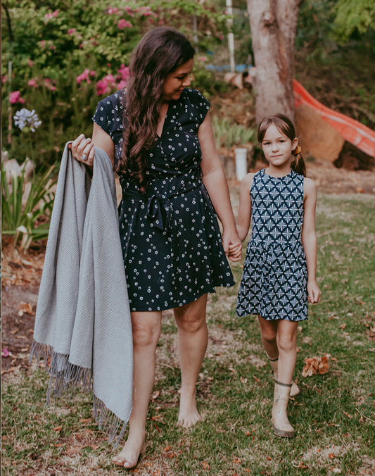Hayley, Earth and Nectar Founder holds hands with daughter Alice both walking through the garden at the farm. Hayley is holding a picnic rug