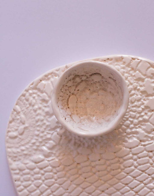 A handmade stoneware platter with lace detail pattern and a small dipping bowl