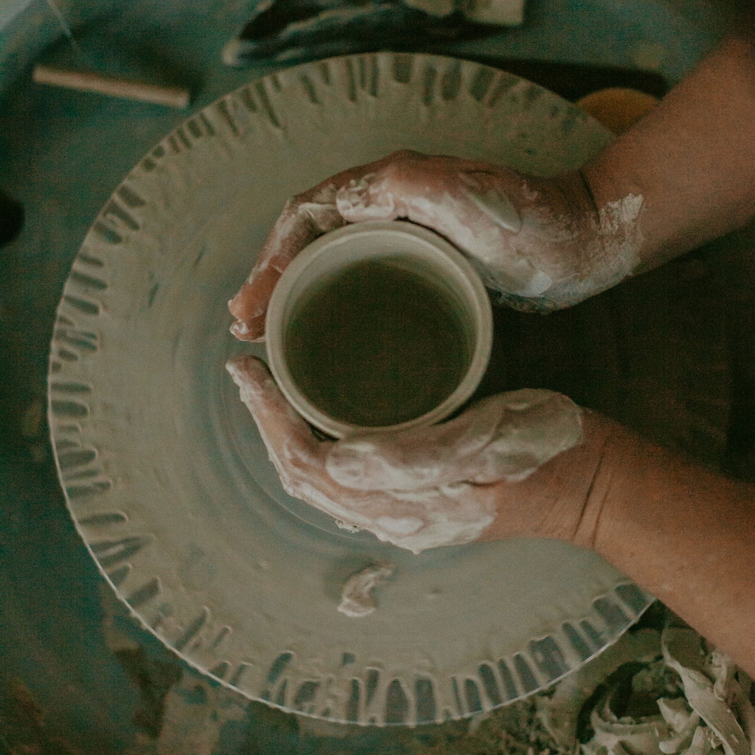 Two hands shaping a stoneware pottery mug on a pottery wheel