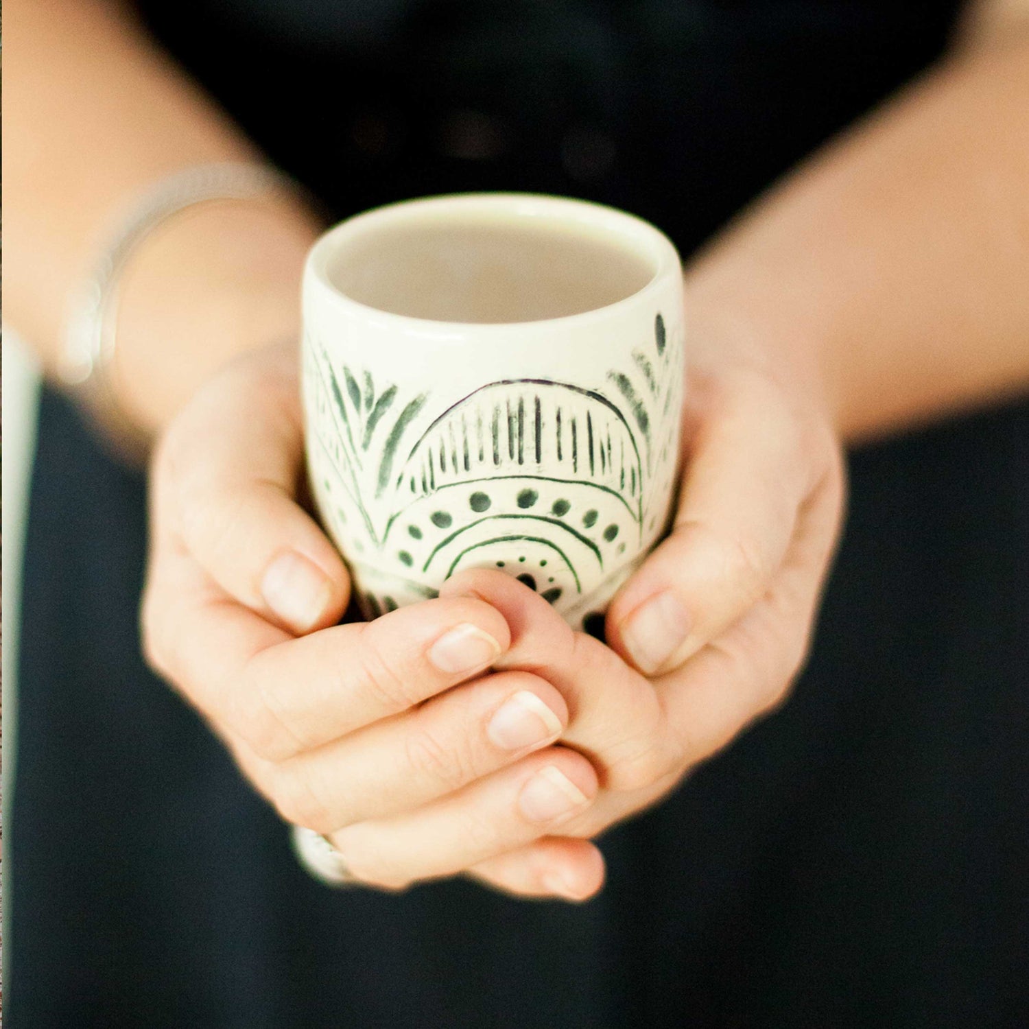 Two hands cup a handmade pottery mug