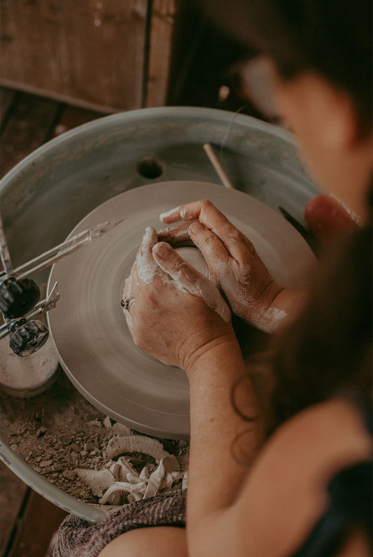 Hayley sitting at the pottery wheel in her studio, her hands guiding the clay into the shape of a mug
