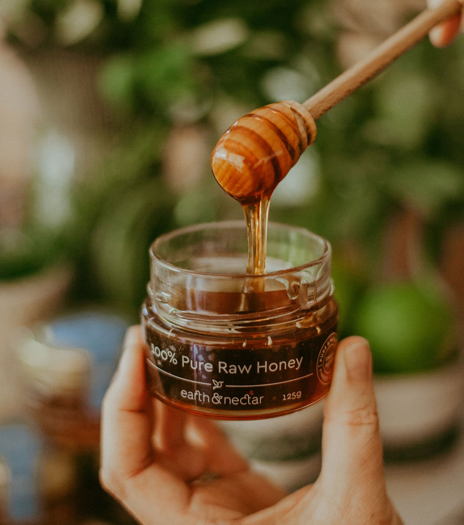 Holding a jar of Earth and Nectar 100% pure, raw honey direct from the Earth and Nectar farm in Roleystone, Perth Western Australia. A honey dipper is being used to show the honey drizzling back into the jar.